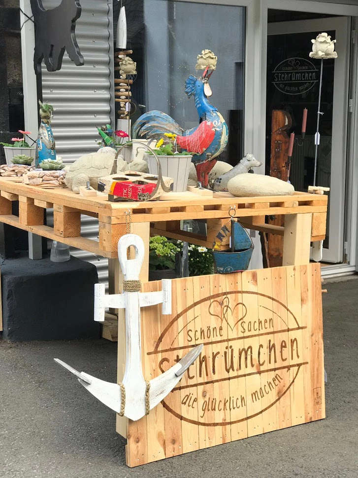 Holzpalette mit verschiedenen Dekoartikeln darunter ein großes weißes Anker-Dekorationsstück und ein Holzschild mit der Aufschrift 'Stehrümchen schöne Sachen die glücklich machen'