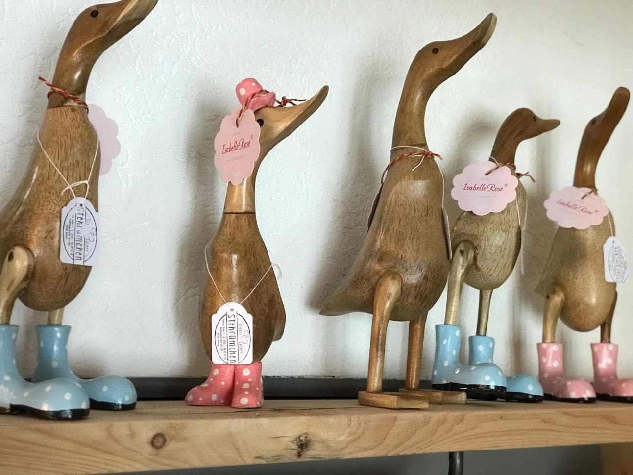 Holzfiguren von Enten mit langen Hälsen, die bunte Gummistiefel tragen und auf einem Regal stehen