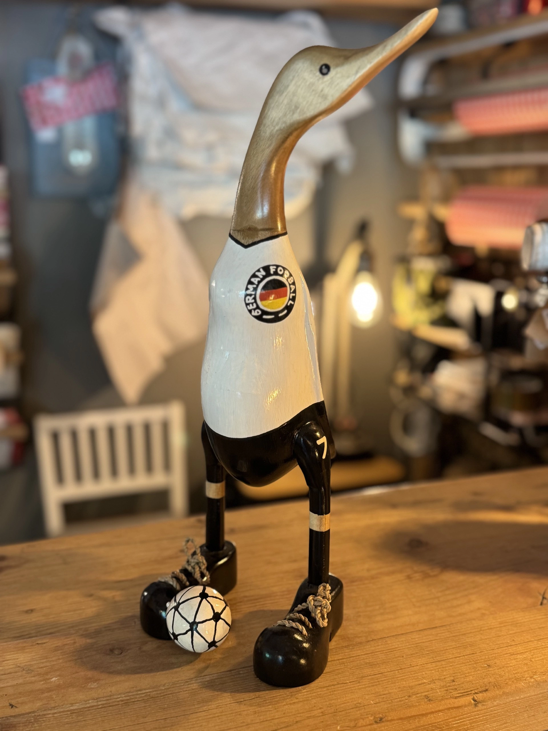Holzfigur einer Gans mit langen Beinen, die schwarze Schuhe und Deutschlandtrikot und -hose trägt und einen Fußball mit dem Aufdruck 'GERMANY FOOTBALL' neben einem Fuß hat